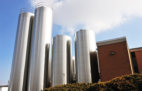 A group of commercial stainless steel tanks and silos for liquid storage, installed outdoors at a modern industrial facility.