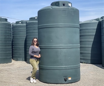 Smiling woman standing beside a large green polyethylene water storage tank in outdoor tank yard