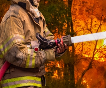 Firefighter spraying water to extinguish raging forest wildfire amid climate change crisis