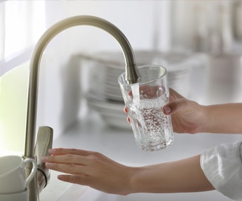 Woman filling glass with clean drinking water from kitchen faucet at home