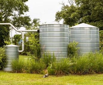 Galvanized steel rainwater harvesting tanks installed in a lush green garden for sustainable water storage