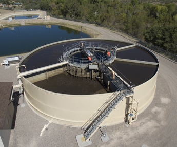 Circular clarifier tank at a modern wastewater treatment facility with sedimentation equipment and operator access platform
