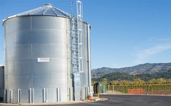 Corrugated steel water storage tank with access ladder installed at a vineyard facility by National Storage Tank Inc. under clear blue sky