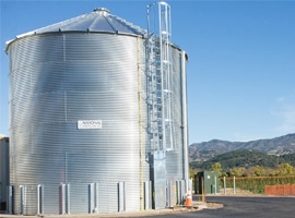 Corrugated steel water storage tank with access ladder installed at a vineyard facility by National Storage Tank Inc. under clear blue sky